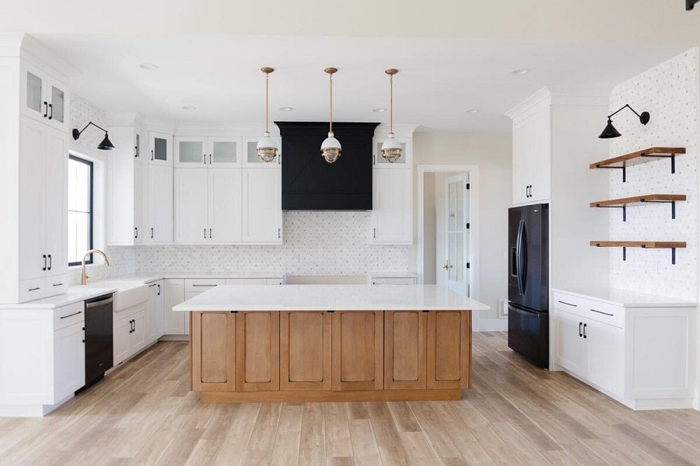 This is a full view of the kitchen that has a large wooden kitchen island that matches with the hardwood flooring and topped with three pendant lights.