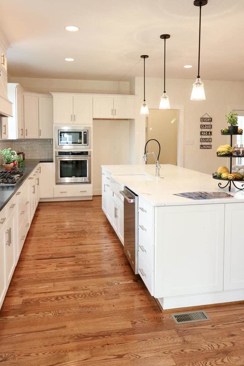 The kitchen features rich hardwood flooring, white cabinetry, and tiled backsplash beautifully contrasted with the black granite countertop.