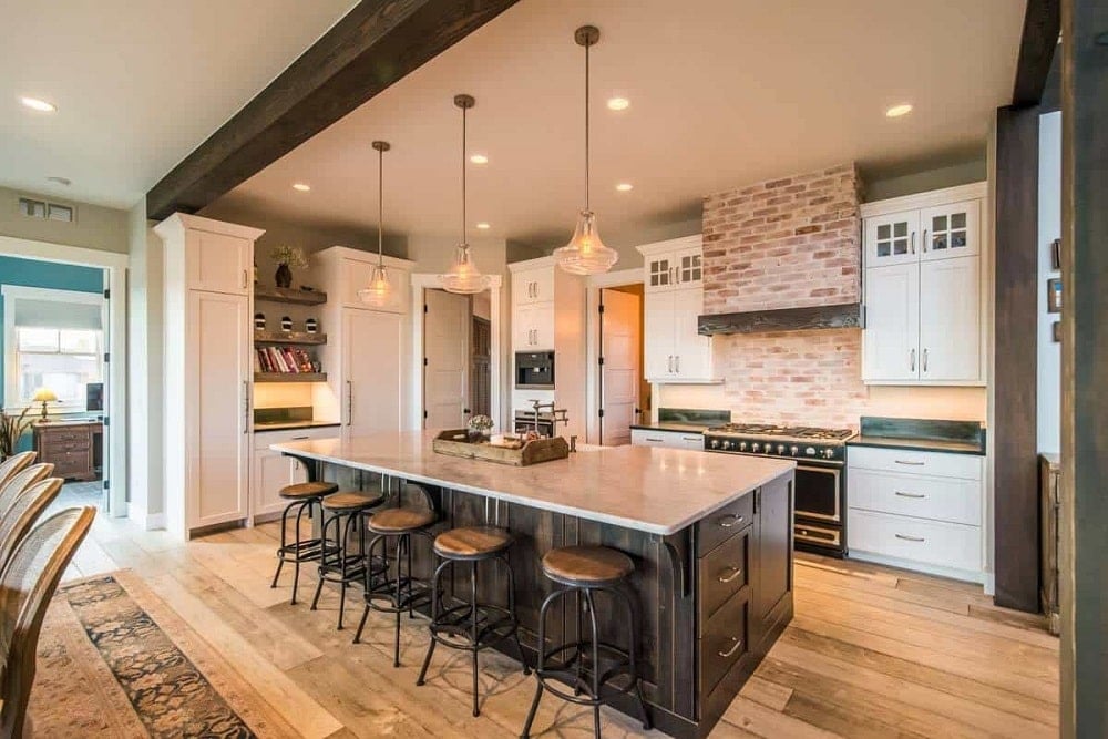 This is a close look at the kitchen that has a large kitchen island with dark cabinetry contrasted by the white countertop topped with pendant lights and paired with stools.