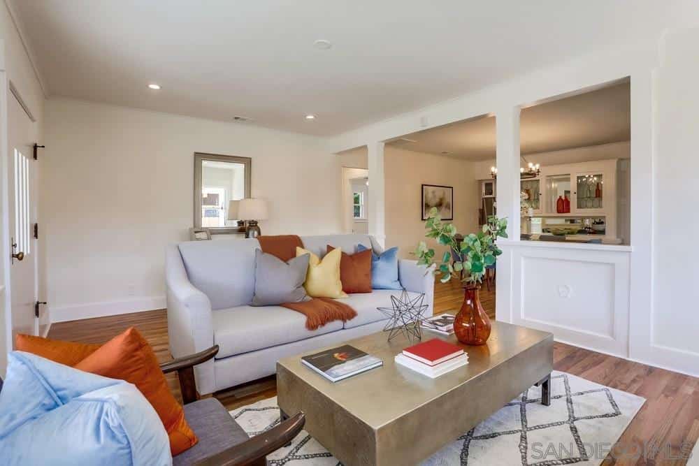 This is an intimate Craftsman-Style living room that makes up for the small floor space with bright walls and ceiling. A brilliant golden coffee table sits atop of a white patterned rug that matches with the light gray sofa and hardwood flooring.