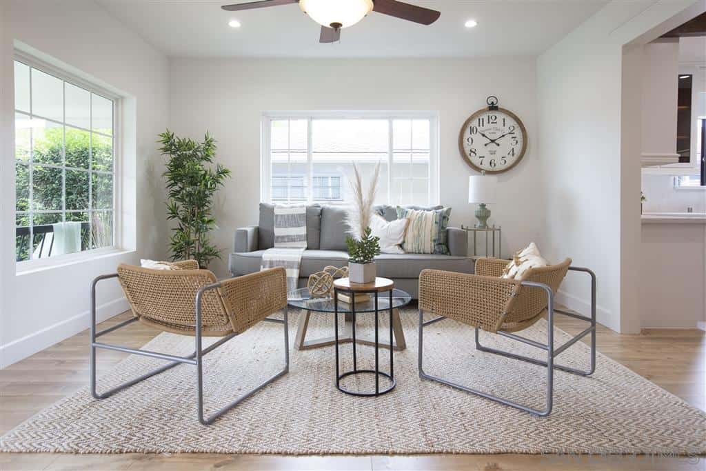 The white walls and massive French windows give this Craftsman-Style living room an illusion of being bigger than it actually is. The hardwood flooring is topped by a patterned area rug that perfectly fits in with the woven wicker chairs and the border of the wall-mounted clock. A touch of warmth and color is brought by the potted plant in the corner.