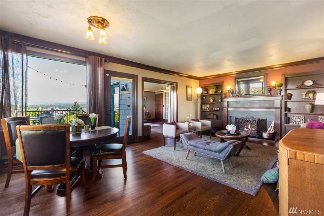 A warm and welcoming fireplace with dark iron grating watches over this Craftsman-Style living room with hardwood flooring topped with a colorful and chic patterned rug. The dark wood elements here complement the walls and ceiling.