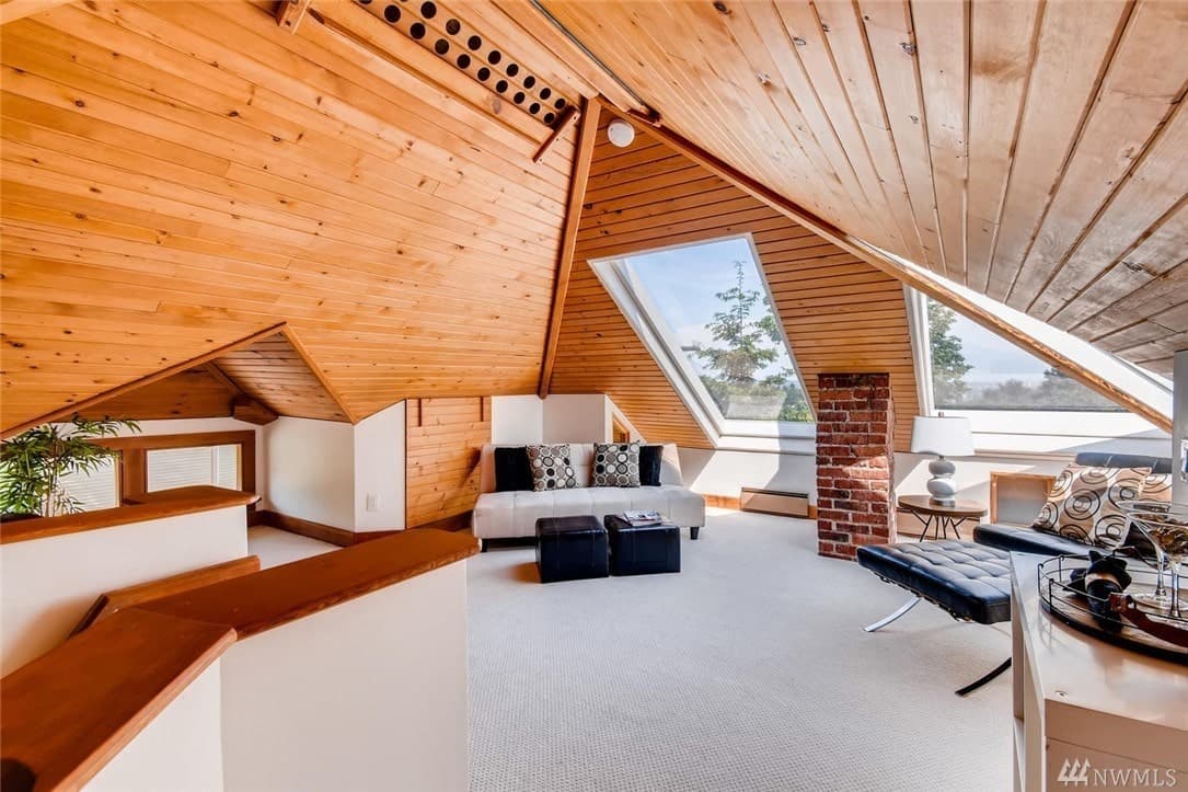 The shiplap arched ceiling of this Craftsman-Style living room offers a cottage-like vibe that still managed to give an open and airy demeanor with its massive glass windows that open to the sky. A lovely brick column stands in between sofas that matches well with the carpeted floor.