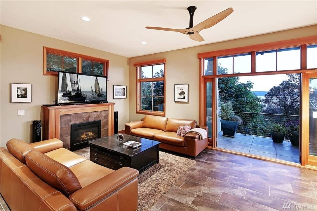 The marble that surrounds the fireplace blends well with the flooring that is topped with a furry rug and an elegant square coffee table with a dark wooden hue. The pair of leather sofas perfectly pairs with the wooden elements surrounding the fireplace, French windows and sliding glass doors.