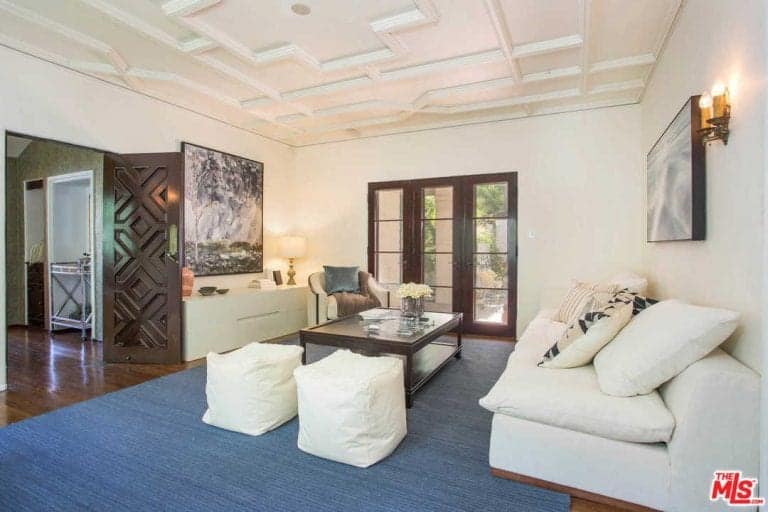 Sophisticated living room features a white sofa with stools and wooden coffee table sitting on a blue rug.