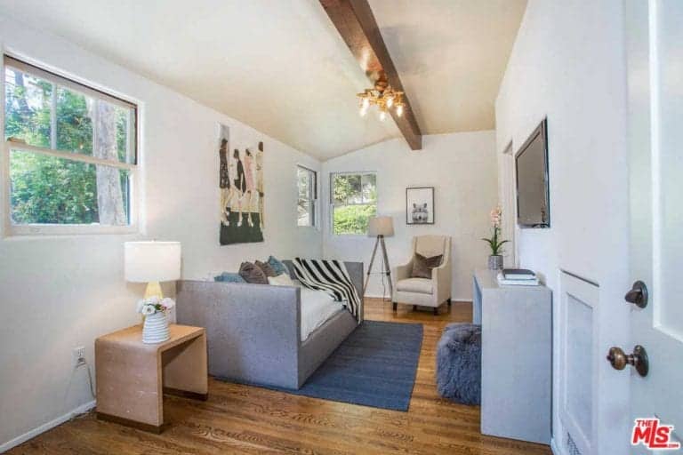Spanish living room with a gray sofa that sits on a blue rug beneath a wall art piece. It is lighted with a brass chandelier that hung from an exposed wood beam.