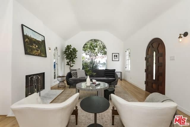 Spanish living room with white walls accented with a dark wood arched door. It includes mismatched sofas and tables creating a cohesive look.