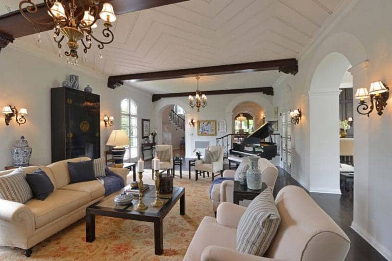 Luxurious living room filled with elegant lights and comfy sofas. It has a zigzag patterned ceiling and hardwood flooring topped with a vintage rug.