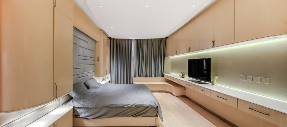 This is a contemporary primary bedroom dominated by the light wooden tones on the hardwood flooring, walls, cabinets and the built-in desk and bench. These are then complemented by the gray elements.