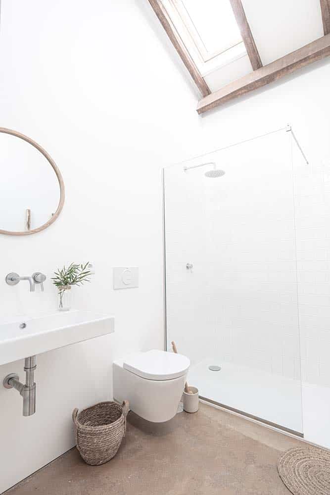 This is a simple bathroom with consistent white walls and porcelain fixtures as well as glass walls. These are then complemented by the rustic elements of the beamed ceiling, and the woven wicker basket on the side of the toilet.