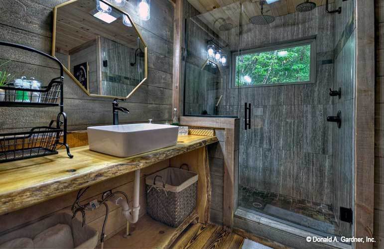 This is the primary bathroom that has a large wooden structure that supports the sink topped with a wall-mounted mirror to pair with the glass door of the shower area on the far side.
