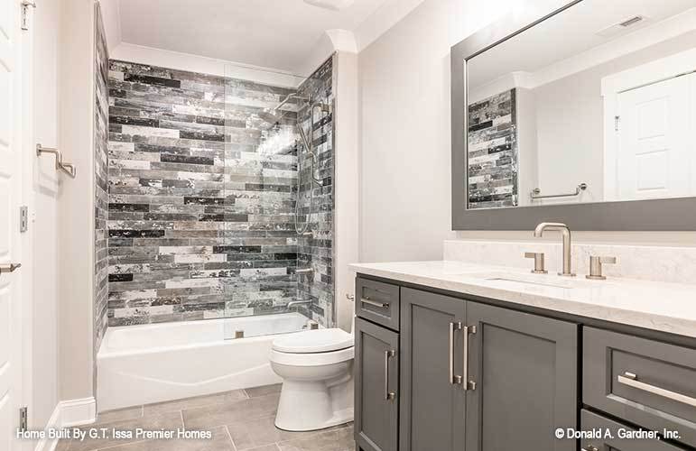 This bathroom offers a marble top vanity, a toilet, and a tub and shower combo accentuated with black linear mosaic tiles.