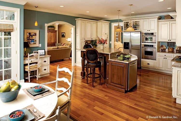 This is an eat-in kitchen with a hardwood flooring to match the brown wooden kitchen island and its stools contrasted by the bright beige cabinetry and stainless steel appliances.