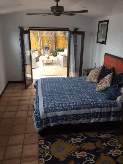 A small and accommodating bedroom that balances its lack of floor space with a door leading to the outside of the house. The brick-colored terracotta flooring also gives it an illusion of being wider while the patterns on the rug and bedspread provide character to the Spanish bedroom.