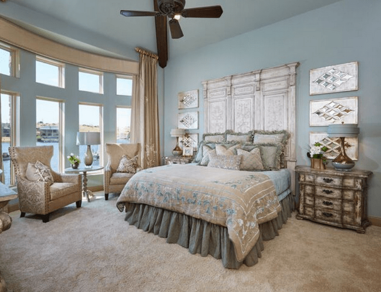 The light hue of the walls provides a good contrast to the silvery headboard that matches the modern wall mounted artwork on either side. The distressed bedside cabinets are an amazing touch that blends perfectly with the beige carpet and single sofa chairs in the reading area.