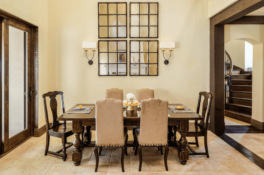 A simple and elegant dining room that is dominated by a set of four wall-mounted modern mirrors flanked by two lamps. Serving as accent are the wooden tones of the wooden beam walkway, glass door boarders and dining table and chairs. The white textured floor contrasts with the smooth white walls and completes the aesthetic.