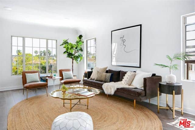 Glass top coffee table sits on a round rug with brown tufted sofa and leather chairs in this stylish living room.