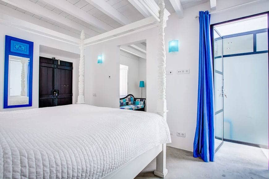 A very bright room with bright white and bright blue colors. The four-poster bed is a good partner to the exposed wooden beams of the ceiling. The added detail of the antique wooden door gives this room a distinctly Spanish character.