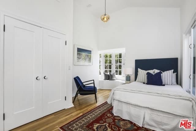 The teardrop lighting paired with the french windows and white walls gives it a modernistic feel. However, the intricately patterned rug brings it back to its Spanish roots. The brilliant addition of navy blue colors into the headboard, chair, and pillow give depth and warmth that balances out the clinical feel of the whiteness.