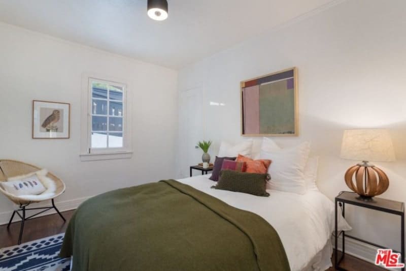 The simplicity of this white Spanish bedroom is its strong suit from the simple color of the walls, the small flush lighting and the small window by the bedside. This simplicity is balanced with a selection of curious details like the brown bedside lamp, the wall-mounted abstract painting above the bed and a patterned rug.