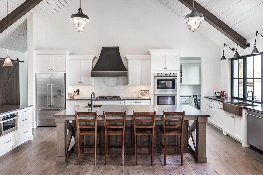 The kitchen has a large kitchen island paired with wooden stools on a hardwood flooring. This is then topped with a white countertop that matches the surrounding cabinetry that makes the stainless steel appliances stand out.