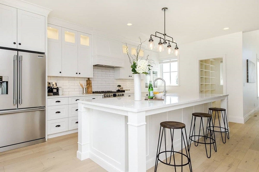 This is a close look at the kitchen that has a large white kitchen island paired with wrought-iron pendant lights that match the stools.