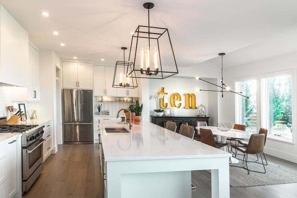 An eat-in kitchen features a marble-top island, white cabinetry, and contemporary pendant lighting.