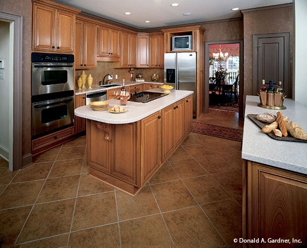 The kitchen has beige flooring tiles to pair with the wooden cabinetry that matches with the kitchen island that has a beige countertop. These elements make the stainless steel appliances stand out.