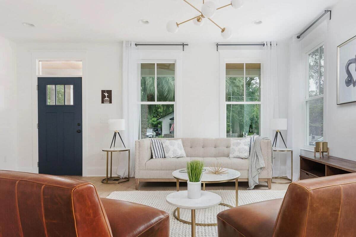 Living room with a tufted sofa, leather chairs, and round tables sitting on a woven area rug.