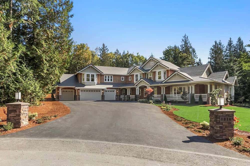 This view of the house showcases the the large concrete driveway towards the house. It has a couple of low decorative stone pillars at the entrance with outdoor lamps.