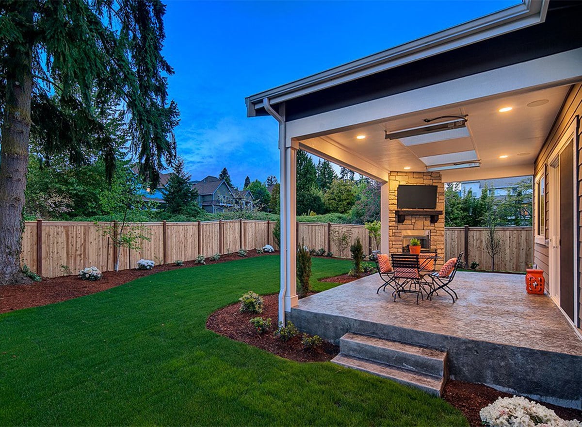 The lush green lawn bordered by plants and wooden fence radiates a serene atmosphere to this backyard.
