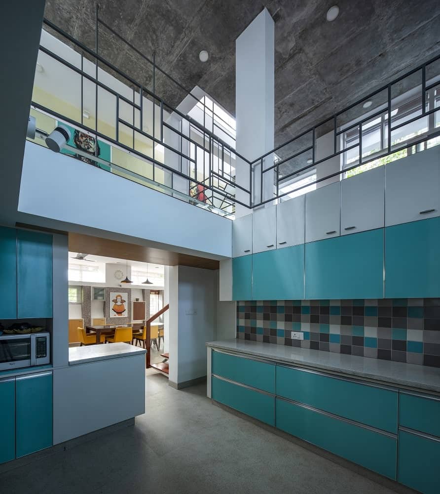 This is a close look at the kitchen that has pastel blue tones to its modern cabinetry lining the walls topped with a tall ceiling and an indoor balcony.