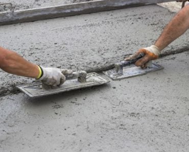 Two workers leveling a concrete surface with trowels.