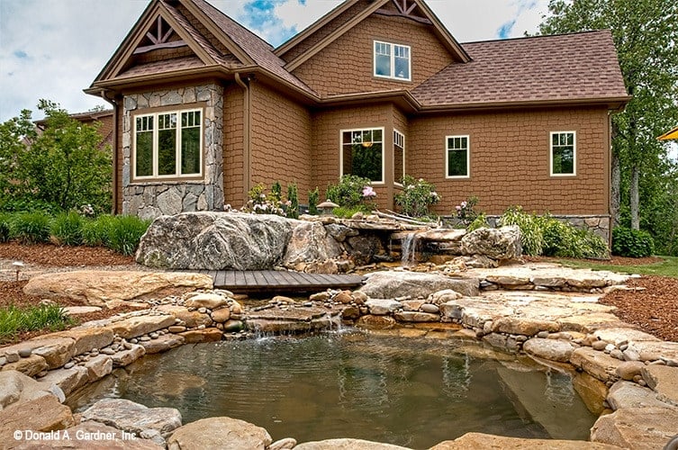 Stone accents in the cedar shake home reflect the stunning man-made pond that's graced with waterfall features and a wood plank deck.