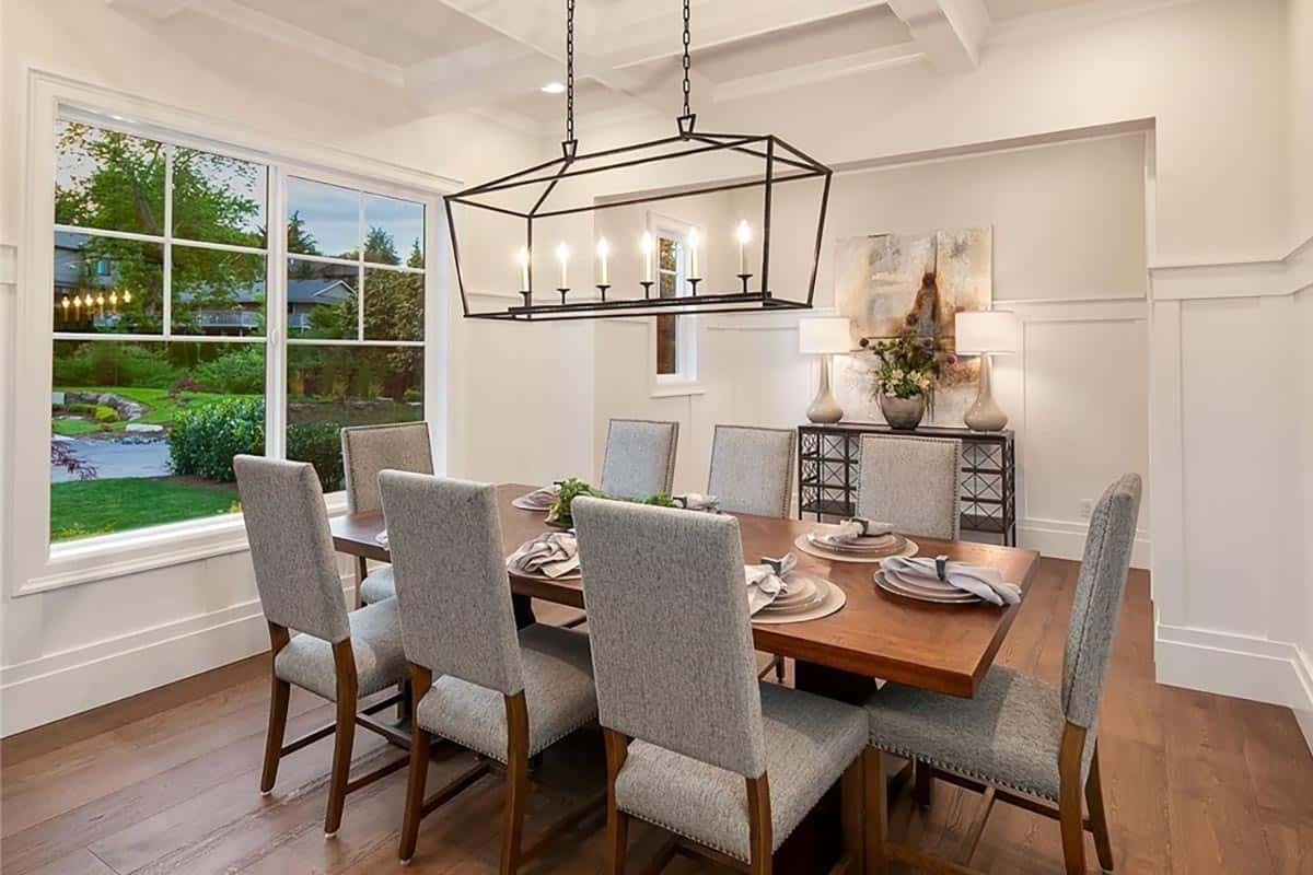 Formal dining room with an 8-seater dining set, half-wainscoted walls, and a coffered ceiling mounted with a linear chandelier.