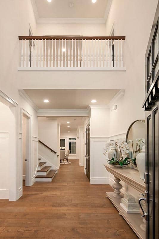 Foyer with a two-story ceiling and a light wood console table topped with decorative vases and a round mirror.