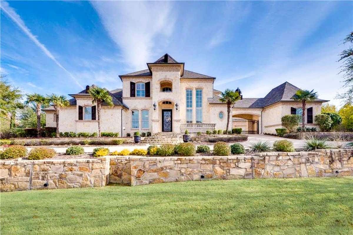 This is the view of the house that showcases the low beige stone wall that surrounds it along with charming shrubs. You can also see here that the houses is complemented by the tall tropical trees in front of it.