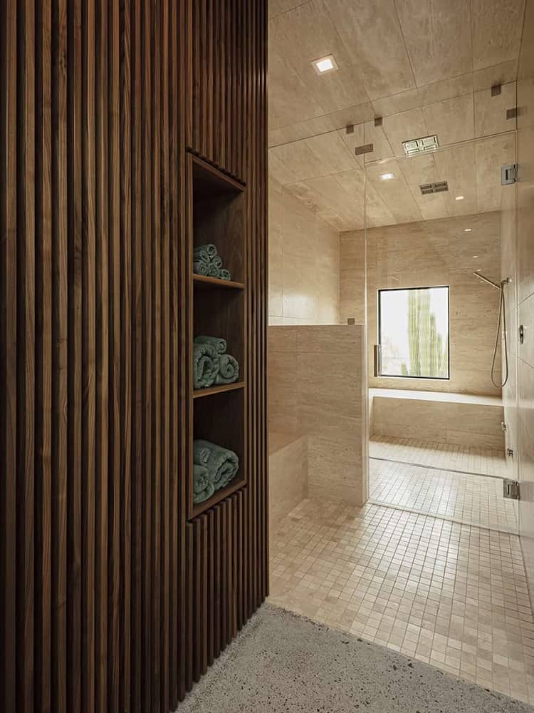 This is a close look at the bathroom that has a consistent earthy beige tone to its floor, walls and ceiling. On the far side is the shower area with its own window and by the entrance is the wooden built-in shelves.