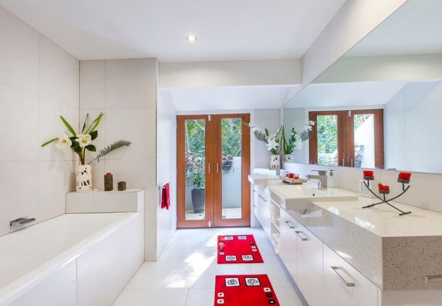 White primary bathroom with Asian-style red rugs. There's a double sink and a deep soaking tub.