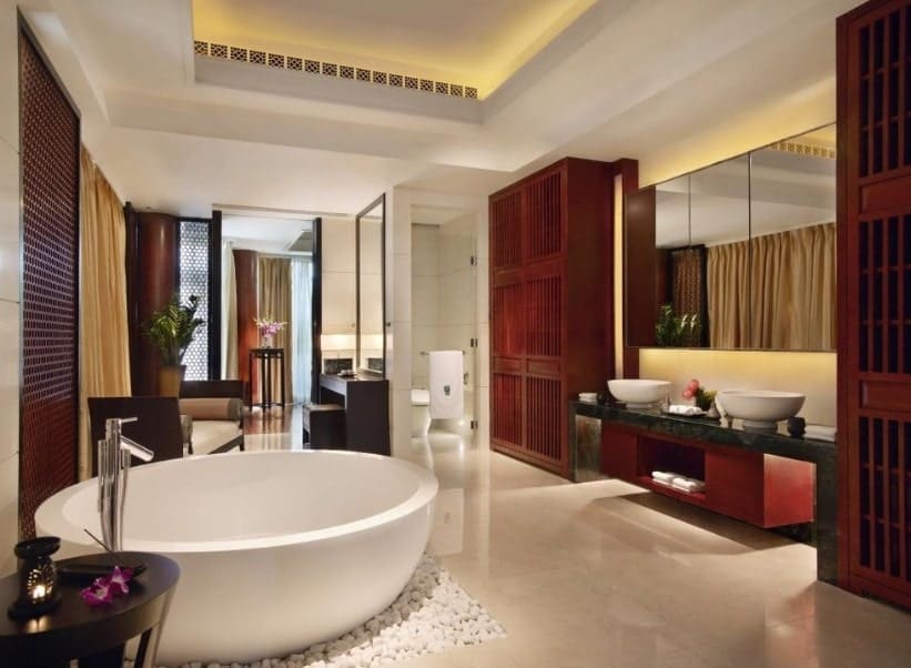 Large and modern Asian-style primary bathroom with a large round freestanding tub along with a powder desk, a toilet room and a walk-in shower. There are two vessel sinks as well. The room has a tray ceiling that has gorgeous lighting.