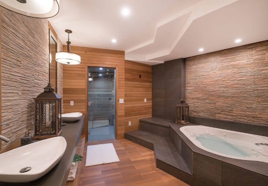 Asian-style primary bathroom with a stunning modish design. It has two vessel sinks lighted by pendant lights along with a drop-in tub under the custom ceiling with recessed lights.