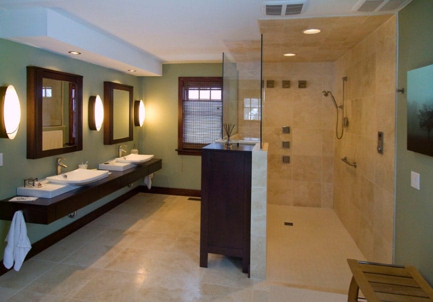 Green primary bathroom with a large walk-in shower and a floating vanity with two sinks, lighted by large round wall lights.