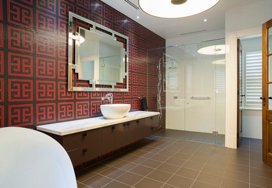 This primary bathroom boasts a decorated wall in Asian style and has a long sink counter with a single vessel sink. The room also offers a walk-in shower room and a freestanding deep soaking tub.