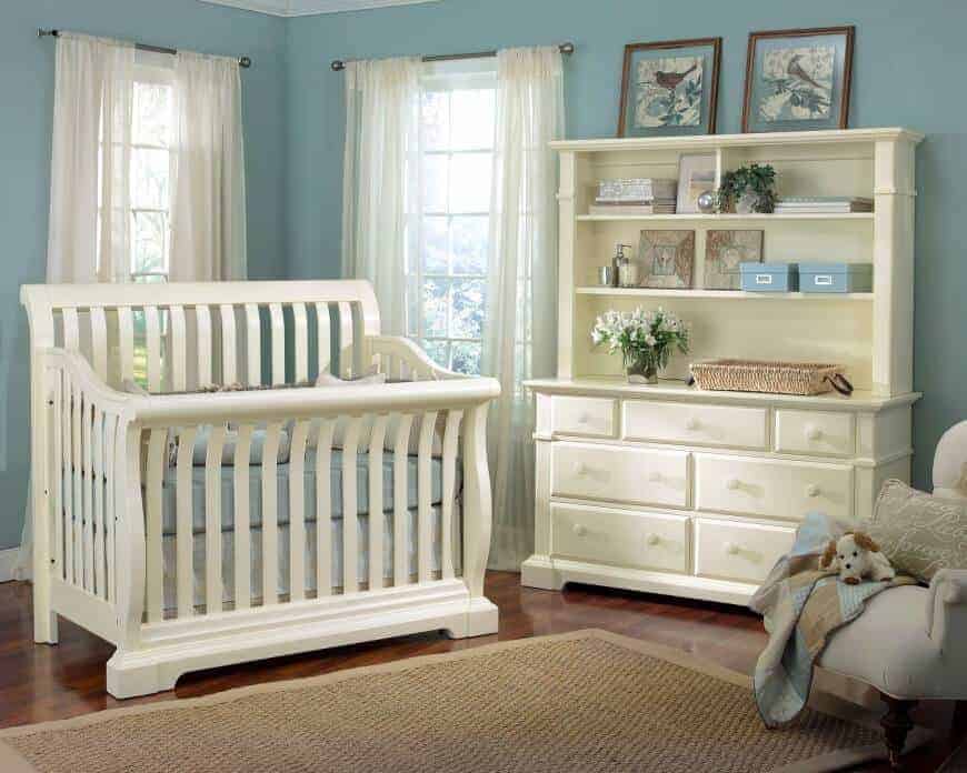 Bird wall arts sit on top of the white cabinet in this nursery boasting a white crib accompanied by an upholstered armchair and jute area rug.