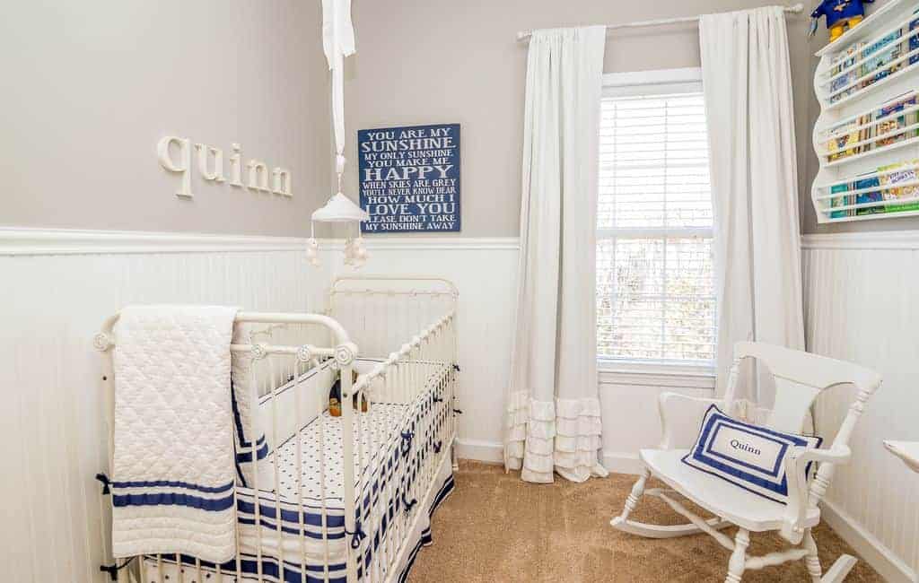 Light and airy nursery with a metal skirted crib that complements the white rocking chair and floating shelf mounted above the beadboard wall.