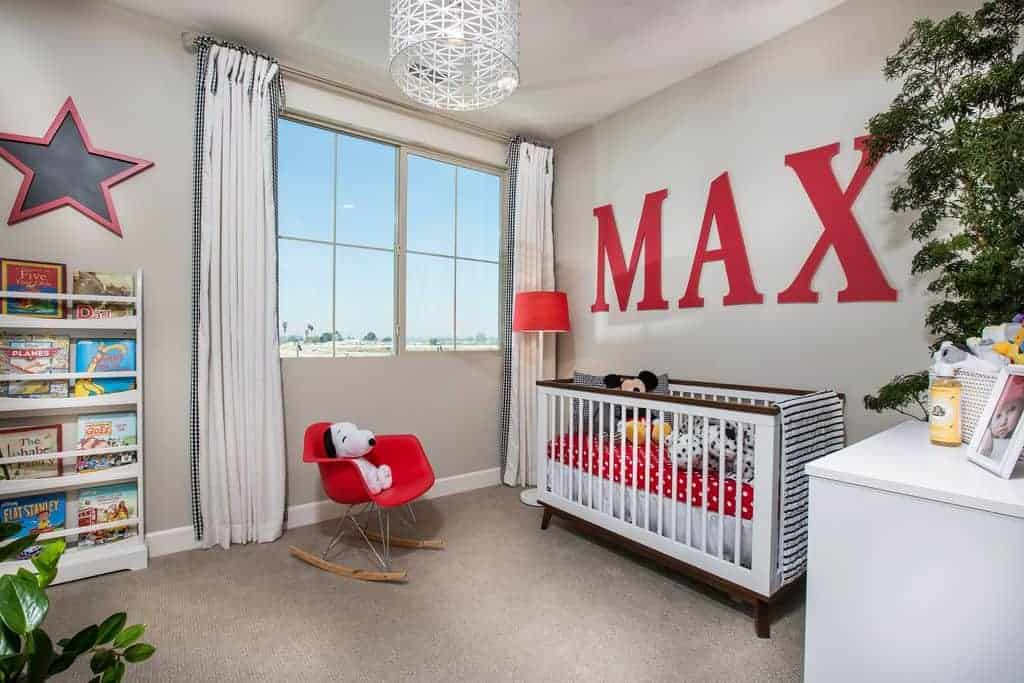 This nursery offers a modern red chair and sleek white crib accented with large, red letters spelling out baby's name. It is illuminated by a stylish drum pendant light and red floor lamp by the glazed windows.