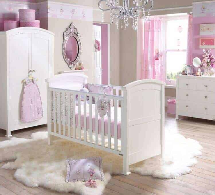 Glamorous nursery decorated with a crystal chandelier and gorgeous mirror mounted next to the arched wardrobe. There's a white crib in the middle that sits on a white faux fur rug over wide plank flooring.