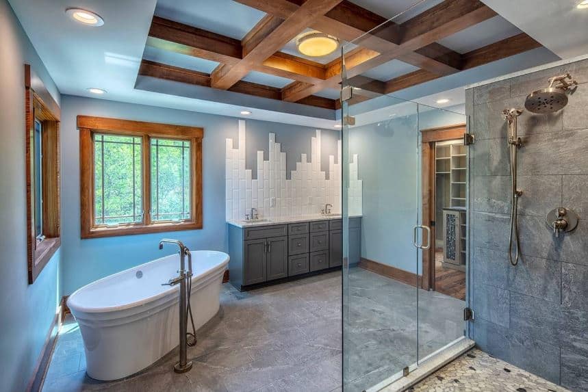 The amazing craftsmanship of this bathroom can be seen on the sleek light blue tray ceiling with a middle tray dominated by wooden exposed beams. This aesthetic is matched with the wood-framed windows on the light blue walls complemented by a gray vanity.