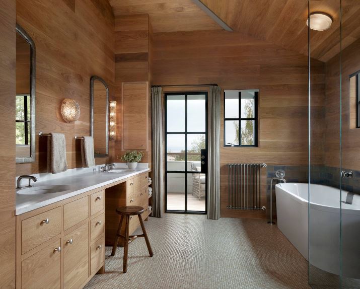 The white freestanding bathtub and the white countertop of the two-sink vanity both stand out against the charming wooden elements of the arched ceiling, walls and wooden vanity paired with beautiful wall lamps and vanity mirrors.