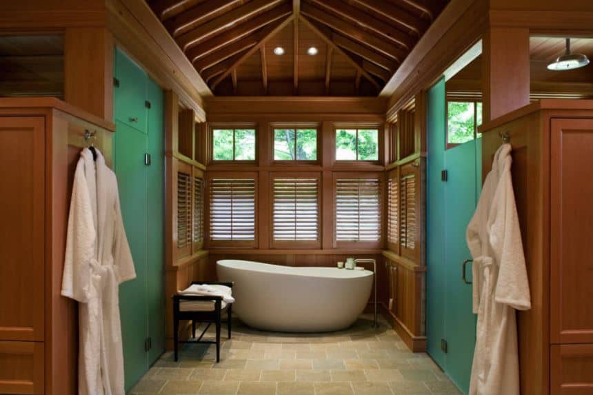 The freestanding white bathtub is placed in an alcove of wooden shuttered windows that blend with the wooden finish of the walls and cathedral ceiling with exposed wooden beams that showcase superb craftsmanship.